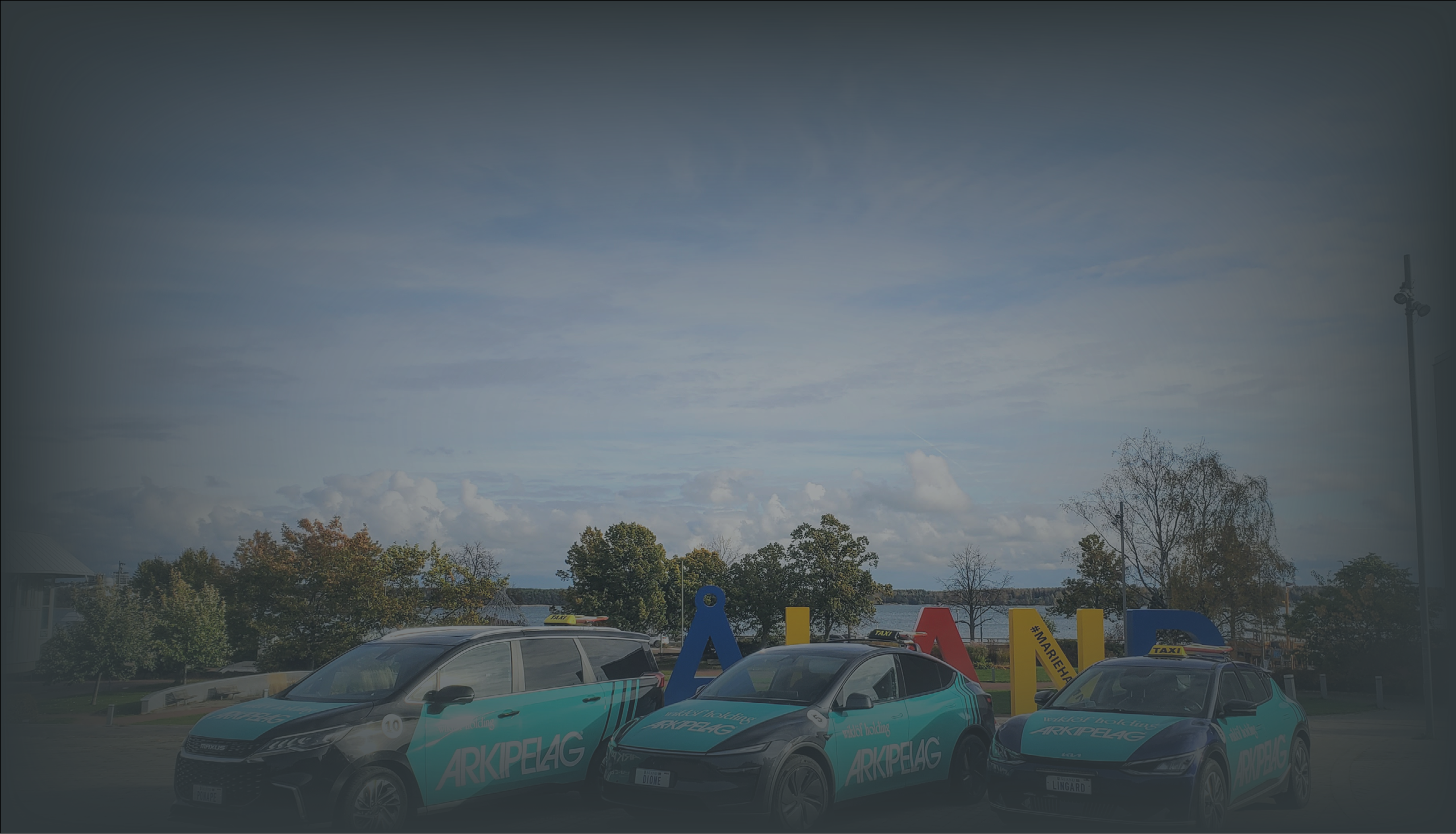 Tre taxibilar framför Ålands-skylten ovanför Miramarparken med utsikt över Slemmern i Mariehamn